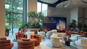 A modern hotel lobby with a large window, a seating area with sofas and chairs, and a large poster on the wall. - Bai Tien Ocean Front Residences (Bac Nha Trang)