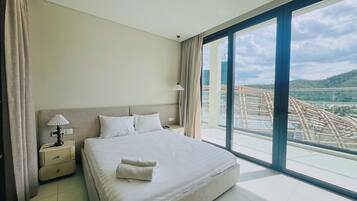 A hotel room with a large bed, a nightstand, a lamp, and a view of a cityscape through a large window.