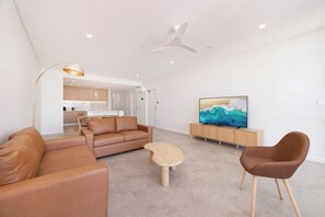 A modern living room with a sofa, chairs, a coffee table, a TV, and a ceiling fan. - Soleil Moreton Bay Apartments (Margate)