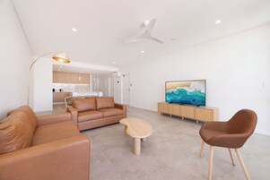 Una sala de estar moderna con un sofá, sillas, una mesa de centro, un televisor y un ventilador de techo.