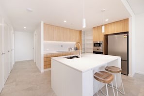 A modern kitchen with a central island, bar stools, wooden cabinets, a stainless steel refrigerator, and a microwave.