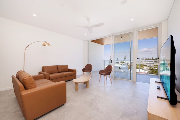 A modern living room with a sofa, chairs, a coffee table, a TV, and a ceiling fan.