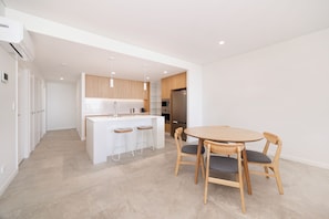 A modern kitchen with white cabinetry, a central island with bar stools, and a dining area with a wooden table and chairs.