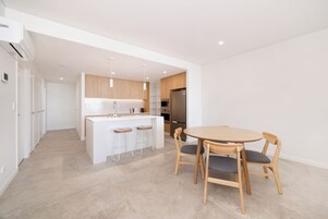Una cocina moderna con armarios blancos, una isla central con taburetes de bar y un comedor con mesa y sillas de madera.