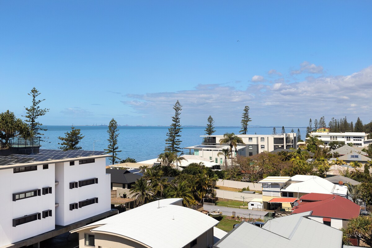 A coastal residential area with modern buildings, a view of the sea, and a clear sky.