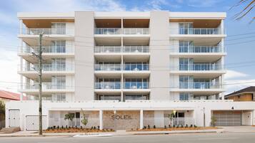 A multi-story building with a white facade, balconies on each floor, and a storefront with the name 'SOLEIL'.