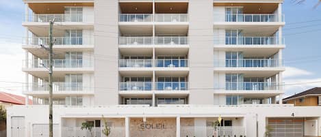 Un edificio de varios pisos con fachada blanca y balcones en cada nivel, y un local comercial con el nombre 'SOLEIL'.