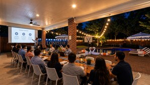 Un groupe de personnes est assis à une table à l’extérieur, devant un écran de présentation.