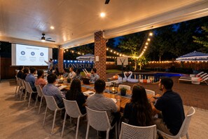 A group of people seated at an outdoor table with a presentation screen in front of them. - Epic TX Stay: Pickleball•Golf Sim•Theater•Sleeps24 (Spring)