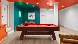 Une table de billard dans une pièce aux murs turquoise et blancs, avec un panneau néon et une œuvre d’art encadrée.