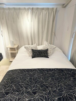 A bed with a patterned bedspread, a pillow with a leaf design, and a bedside table with a lamp. - Amazing 1bedroom apartment with AC in lovely 台東区 (台東  区)