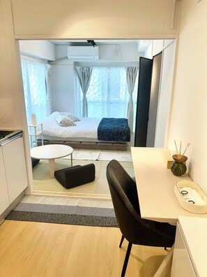 Ein kleines Zimmer mit Bett, einem Tisch, einem Stuhl und einer Küchenzeile.