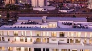 Ett hotell med flera våningar, ett platt tak, stora fönster och utsikt över stadens silhuett.