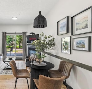 A dining area with a round table, chairs, and a hanging light fixture. - Luxury Rockies Escape - Pool & HotTub - King Bed - AC! (Canmore)