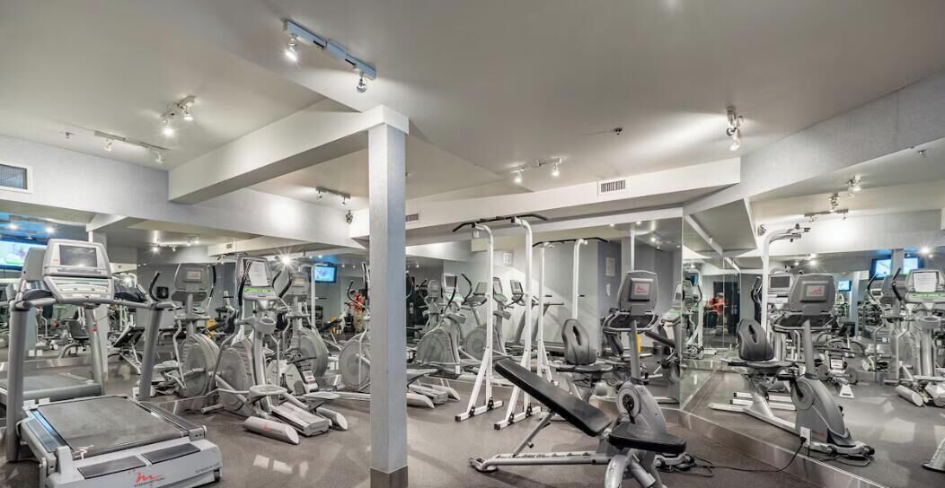 A gym with various exercise machines, mirrors, and a large mirror wall.