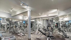 Un gimnasio con diferentes máquinas de ejercicio, espejos y una amplia pared de espejos.