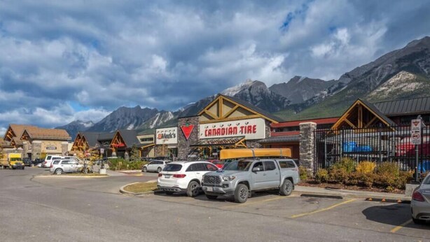 Un estacionamiento con varios coches, una tienda Canadian Tire y montañas al fondo.