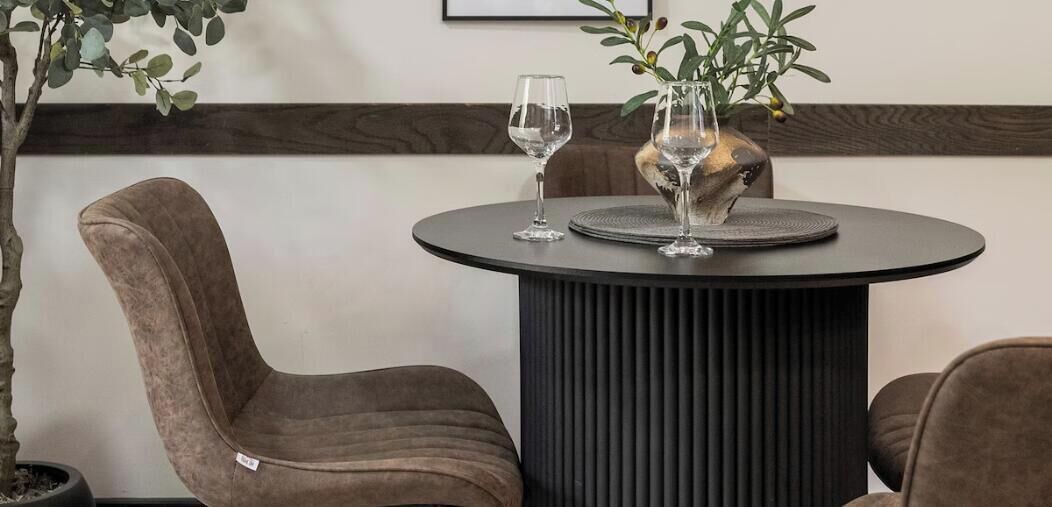 A round table with two wine glasses and a decorative vase, surrounded by upholstered chairs.