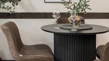 A round table with two wine glasses and a decorative vase, surrounded by upholstered chairs.