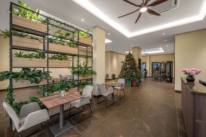 Un ambiente interno moderno con un'unità di scaffalatura in legno piena di piante, un albero di Natale e una reception con un vaso di fiori.