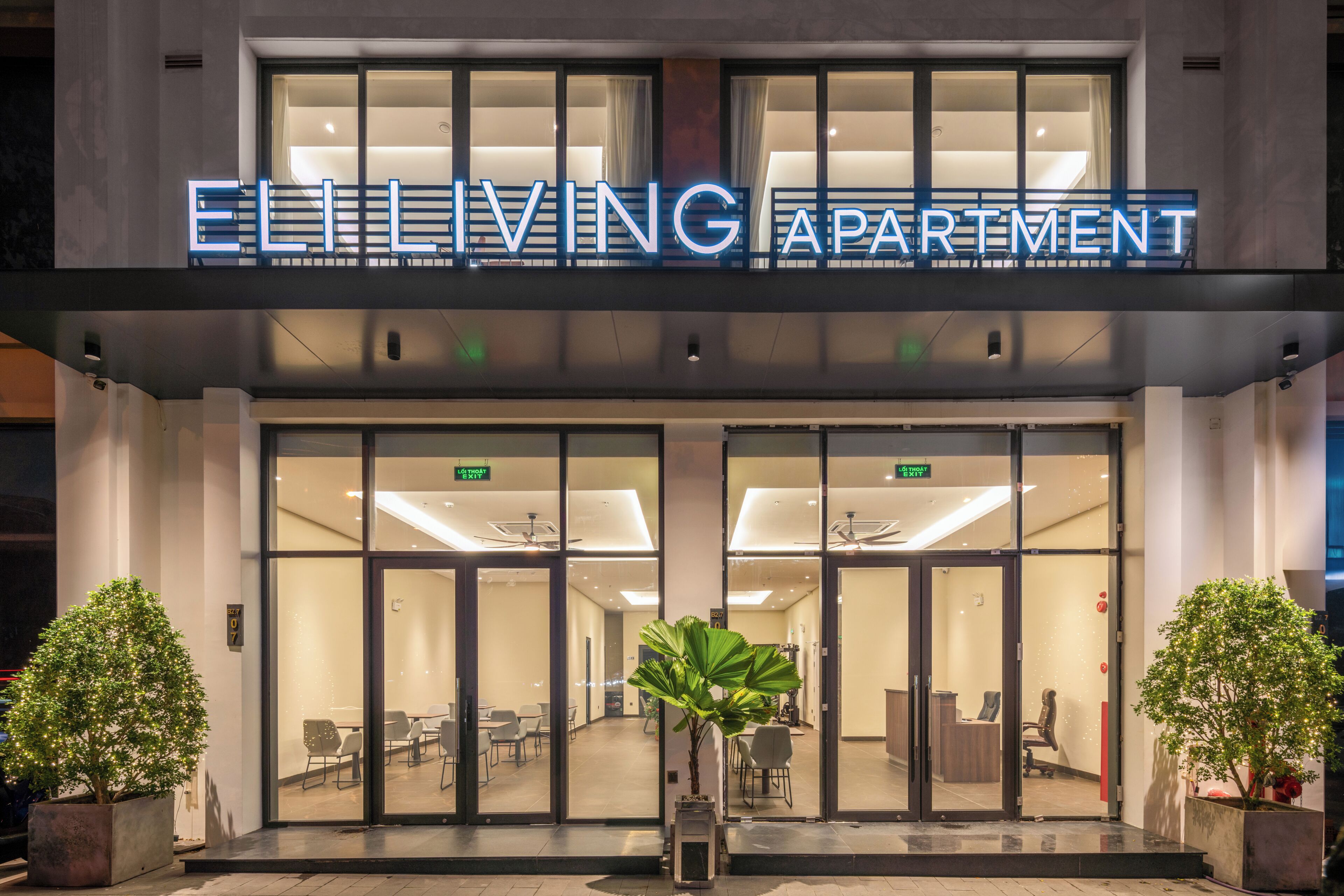 The exterior of Eliving Apartment with a modern design, featuring glass doors and a sign above the entrance.