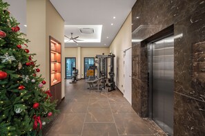Un couloir décoré d’un sapin de Noël, doté d’un ventilateur de plafond, d’un espace de remise en forme avec des appareils d’exercice et d’un ascenseur en marbre.