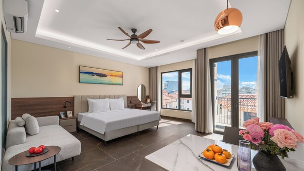 Habitación de hotel con cama, sofá, escritorio, vistas de la ciudad y un balcón con flores.