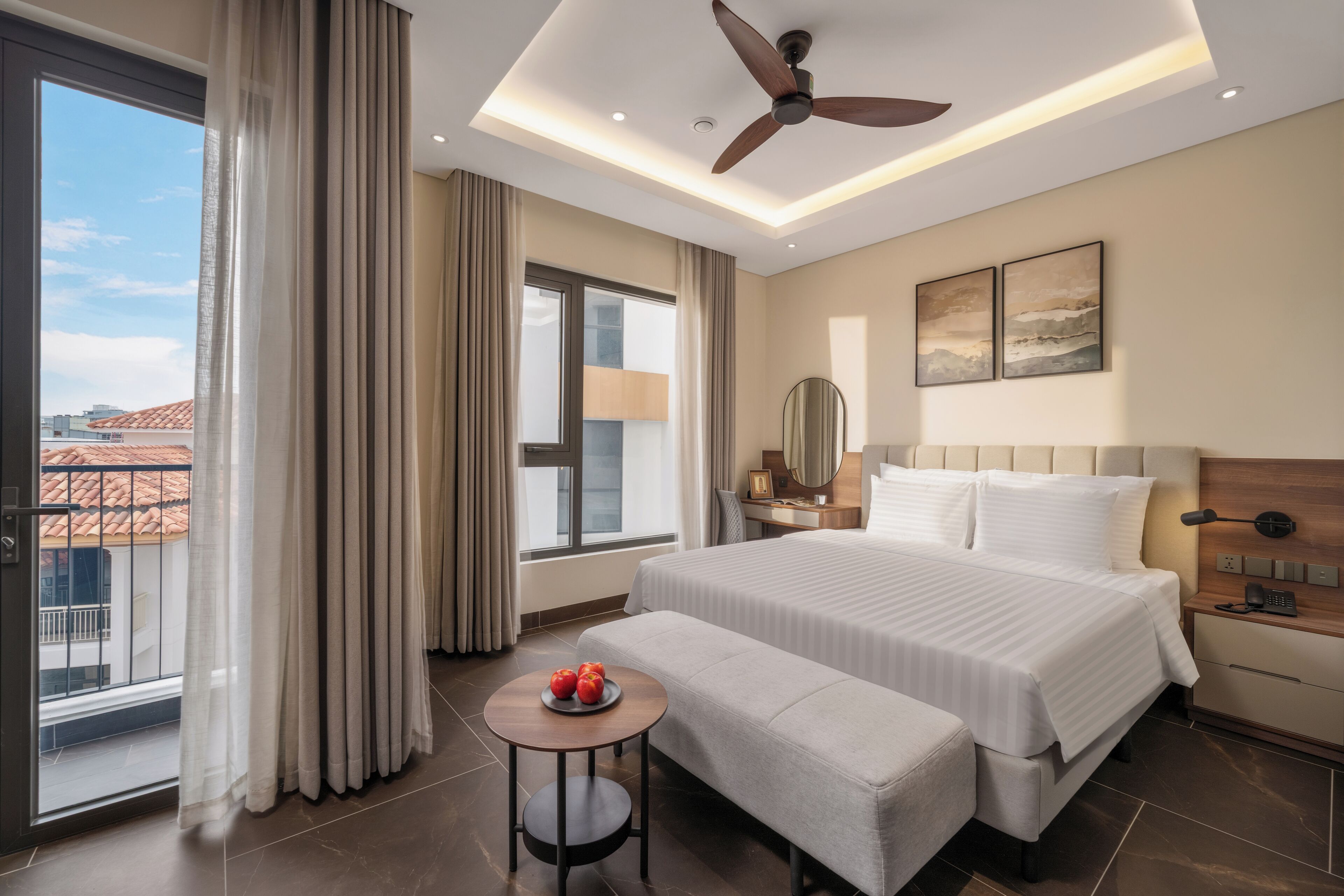 A hotel room with a bed, bedside table, lamp, and a view of the city.