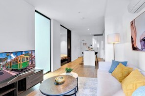 Una sala de estar moderna con una televisión de pantalla plana, un sofá, una mesa de centro y una cocina al fondo.