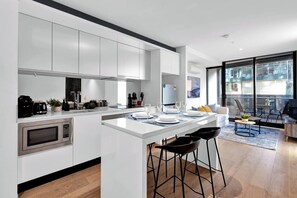 Una cocina moderna con armarios blancos, una isla central con taburetes y un comedor con una mesa dispuesta para dos.