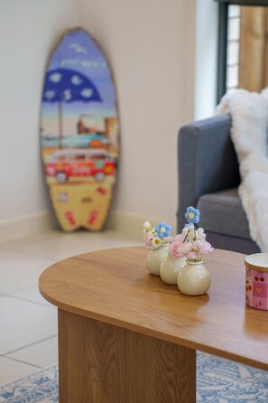 A wooden coffee table with a vase of flowers and a surfboard decoration in the background.