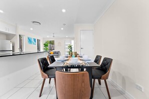 Une cuisine moderne avec des meubles blancs, un plan de travail noir et un coin repas comprenant une table en bois et des chaises noires.