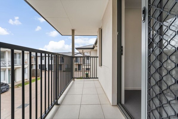 A balcony with a metal railing, a tiled floor, and a view of adjacent buildings.