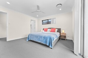 Quarto com cama, mesa de cabeceira, ventilador de teto e janela com persianas.