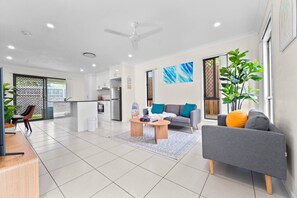 A modern living room with a grey sofa, a coffee table, and a dining area with a kitchen in the background.