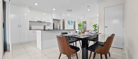 Una cocina moderna con armarios blancos, una mesa de comedor con sillas y una puerta blanca.