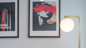 En grön soffa med en mönstrad, brun kudde, ett inramat konstverk ovanför och en golvlampa med en rund lampskärm.