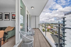 A balcony with a view of a cityscape, a green sofa, and two wicker chairs. - Valley Stay Stylish Apartment |Parking |Pool & Gym (Newstead)