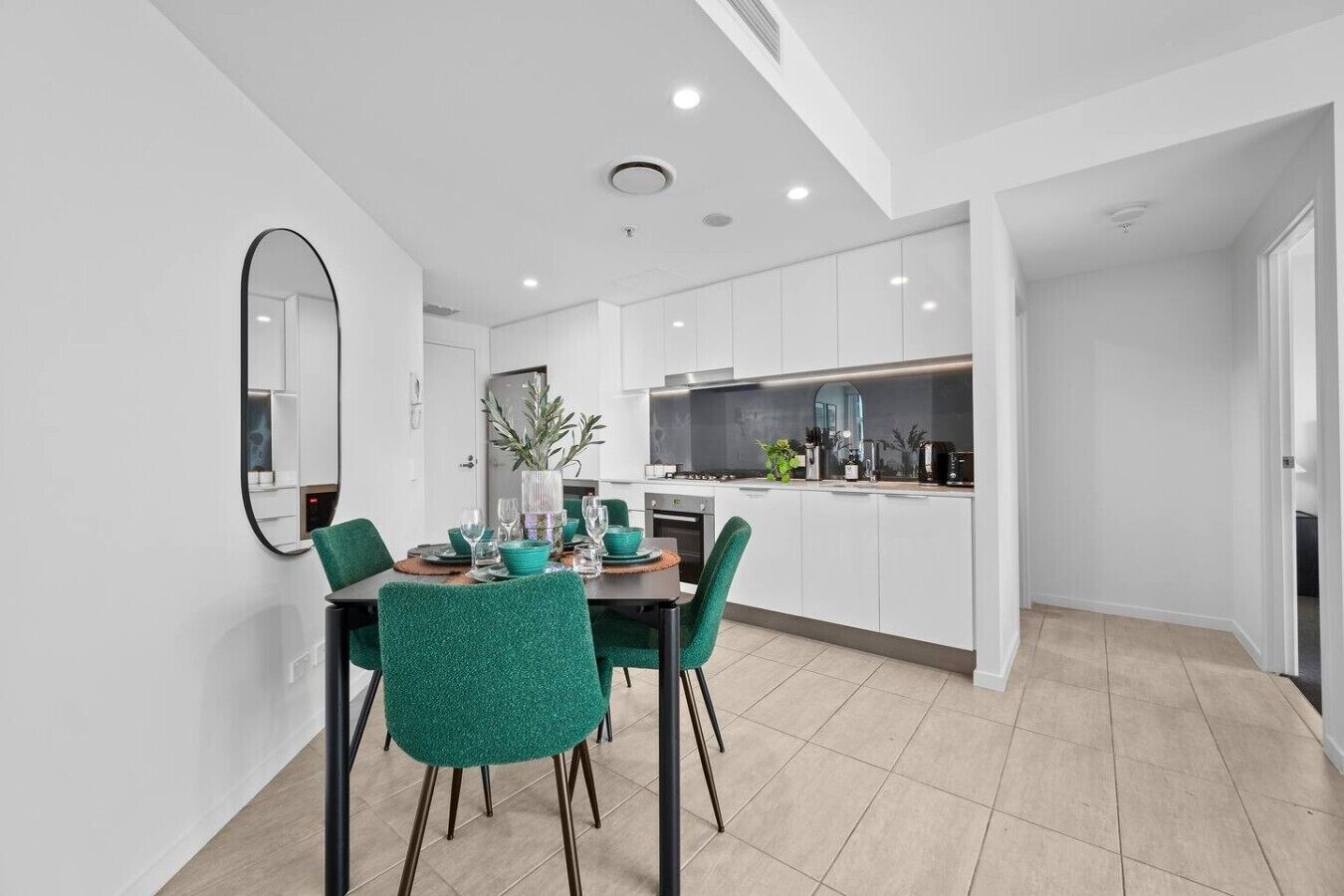 A modern kitchen with white cabinets, a dining area with teal chairs, and a large mirror on the wall.