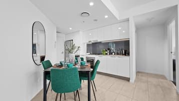 A modern kitchen with white cabinets, a dining area with teal chairs, and a large mirror on the wall.