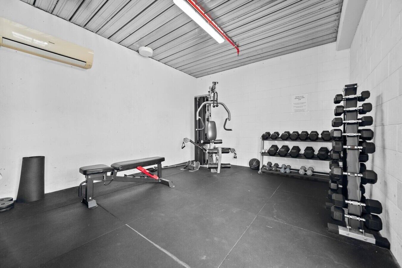 A gym with a bench, squat rack, and dumbbells.