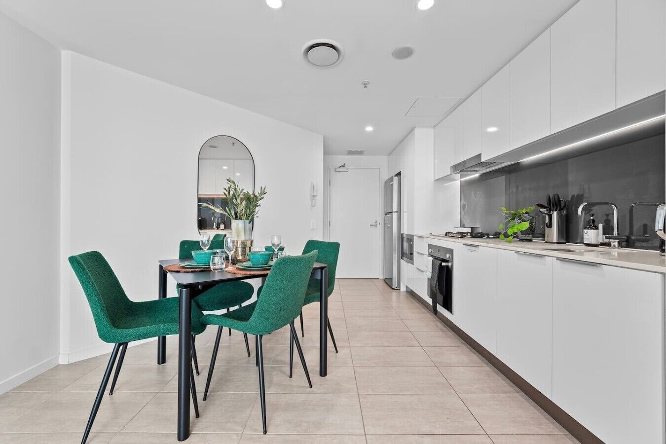 A modern kitchen with white cabinetry, a dining area with green chairs, and a large window.