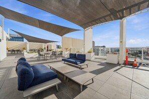 Eine Dachterrasse mit Sitzgelegenheiten im Freien, einem überdachten Bereich und Blick auf die Skyline.