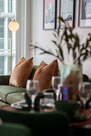 A living room with a green sofa, two brown cushions, a vase with greenery, and a floor lamp. - Valley Stay Stylish Apartment |Parking |Pool & Gym (Newstead)