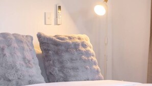 A bed with white bedding, two grey pillows, a white floor lamp, and a wall-mounted light switch. - Great Value Renoted Studio| Near Griffith & Shops (Nathan)