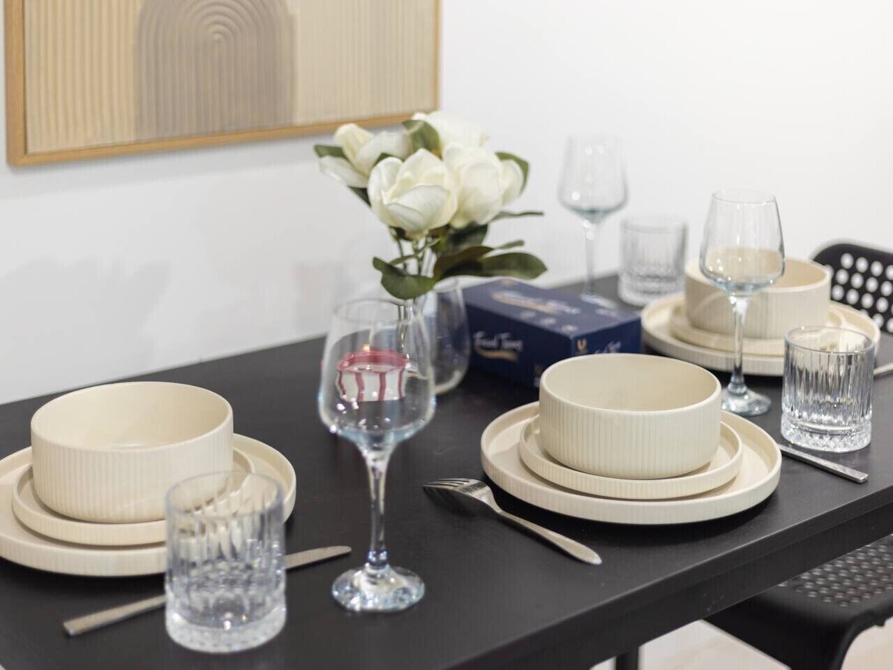 Une table à manger dressée avec de l’assiette, des bols et des verres blancs, agrémentée d’un vase rempli de fleurs blanches.