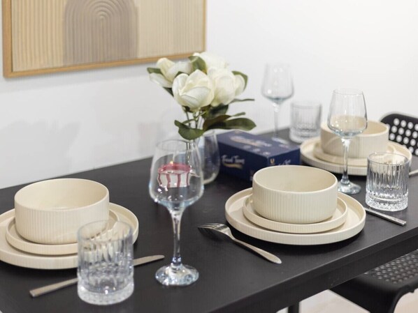 A dining table set with white plates, bowls, and glasses, accompanied by a vase of white flowers.