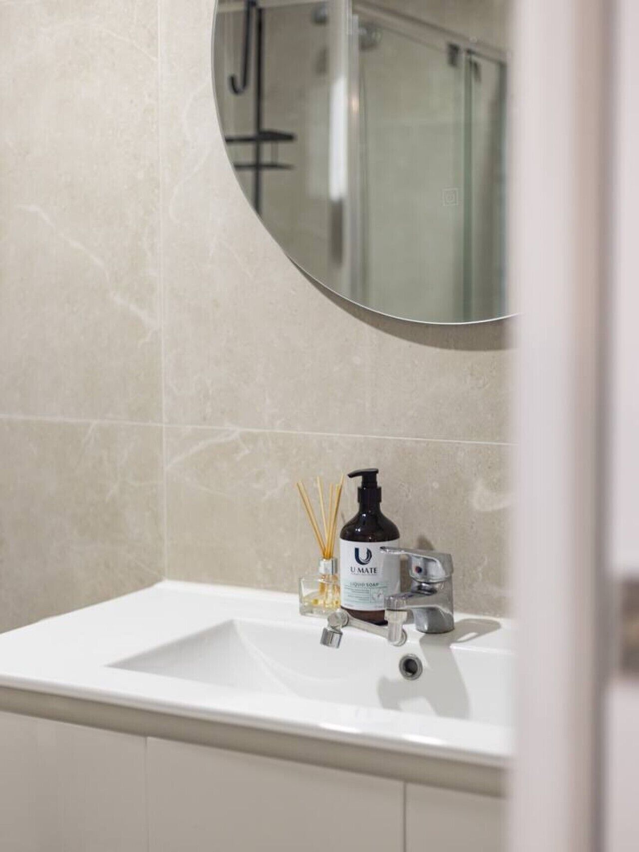 Un baño con un lavabo blanco, un espejo redondo y una botella de jabón líquido U-MATE.