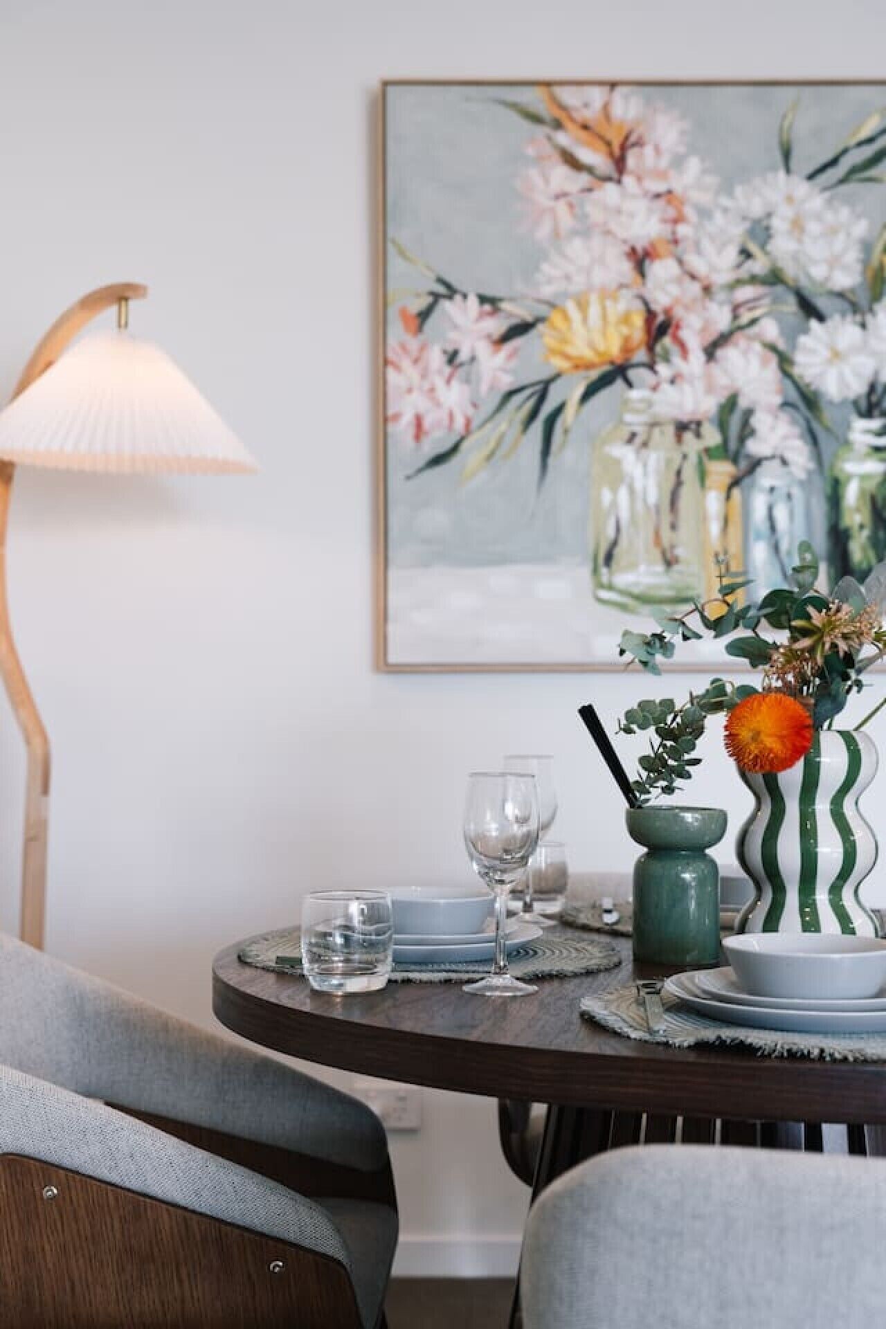 A dining table with a vase of flowers, a lamp, and a painting on the wall.
