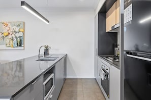 A modern kitchen with a stainless steel sink, a built-in oven, and a black refrigerator.
